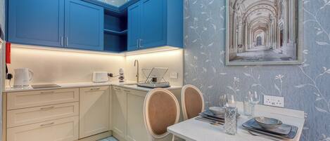A modern kitchen with blue cabinets, a dining table with chairs, and a decorative wall with a framed picture.
