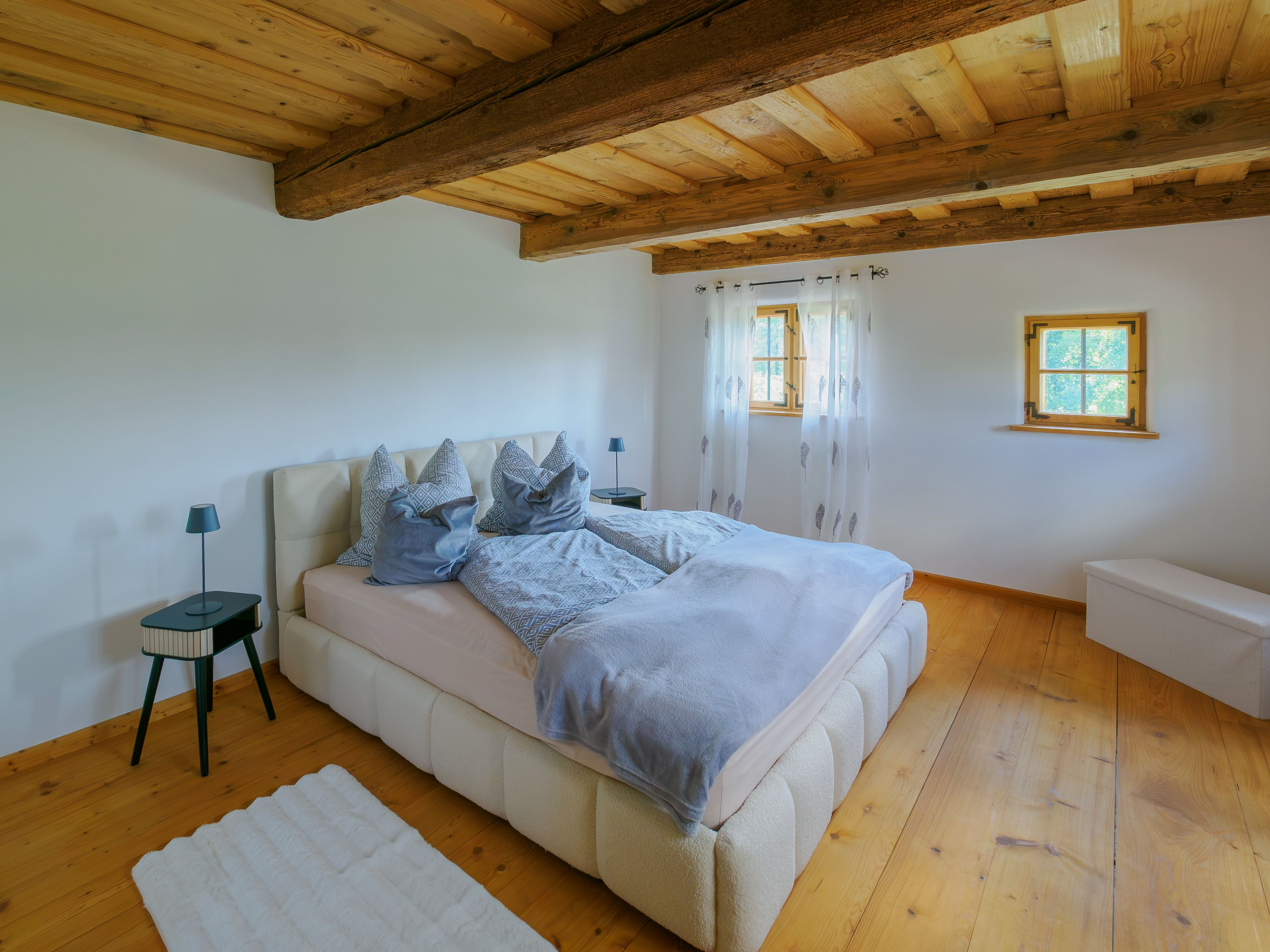 Une chambre à coucher avec un lit, des tables de chevet, une fenêtre et un plafond en bois.