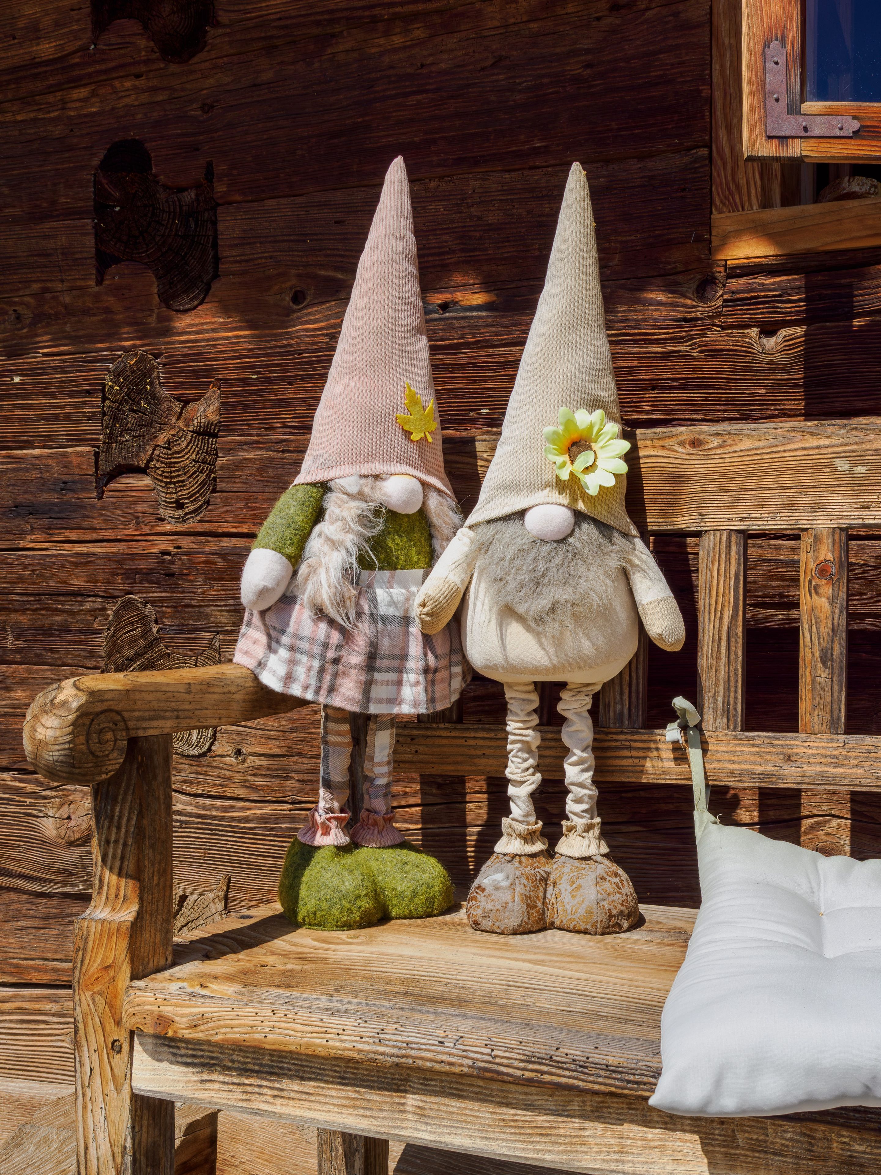 Deux statuettes de gnomes sont assises sur un banc en bois, avec un décor rustique en arrière-plan.