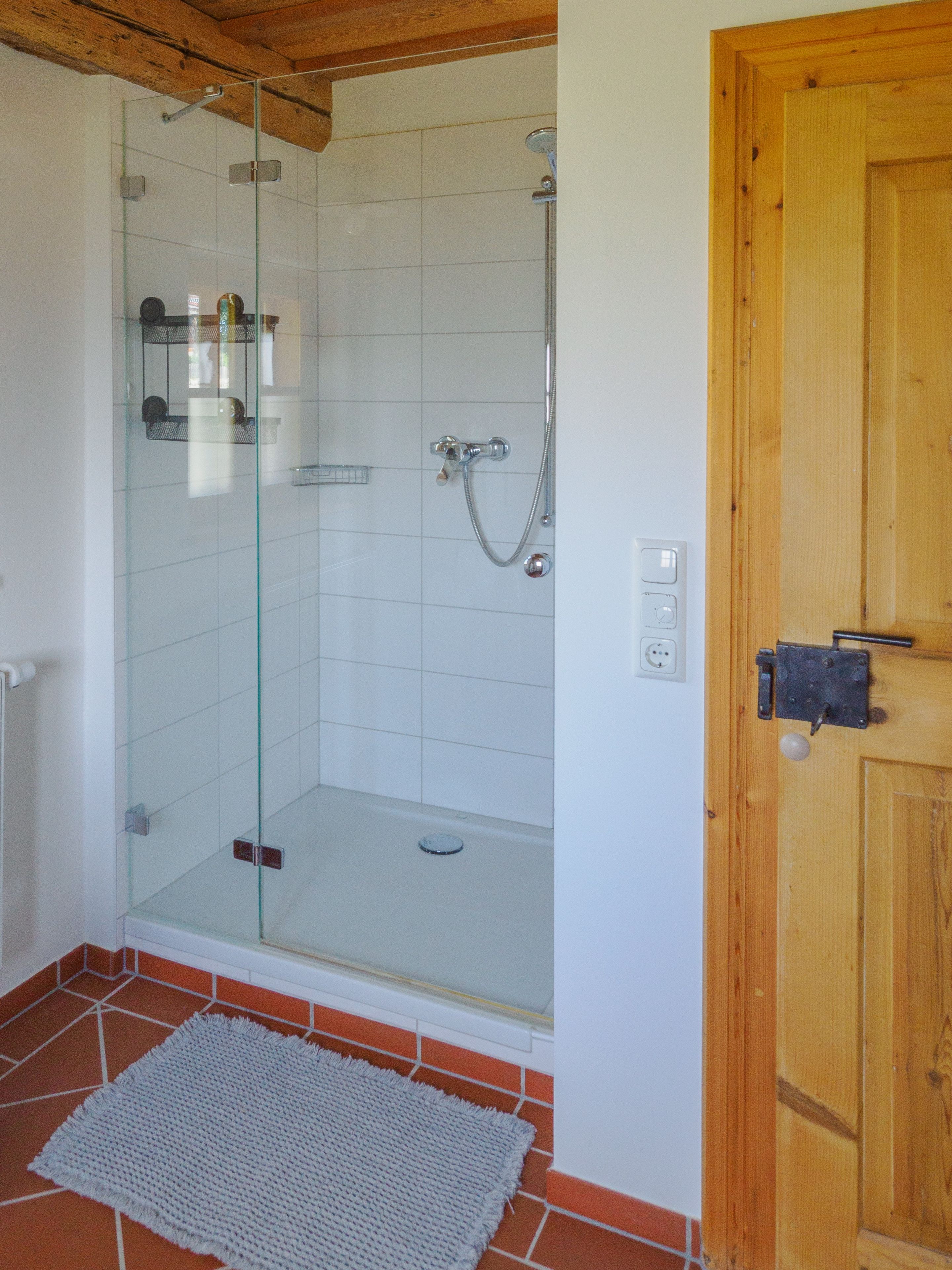A shower with a glass door, a wooden door frame, and a tiled floor.