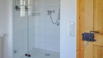 A shower with a glass door, a wooden door frame, and a tiled floor.