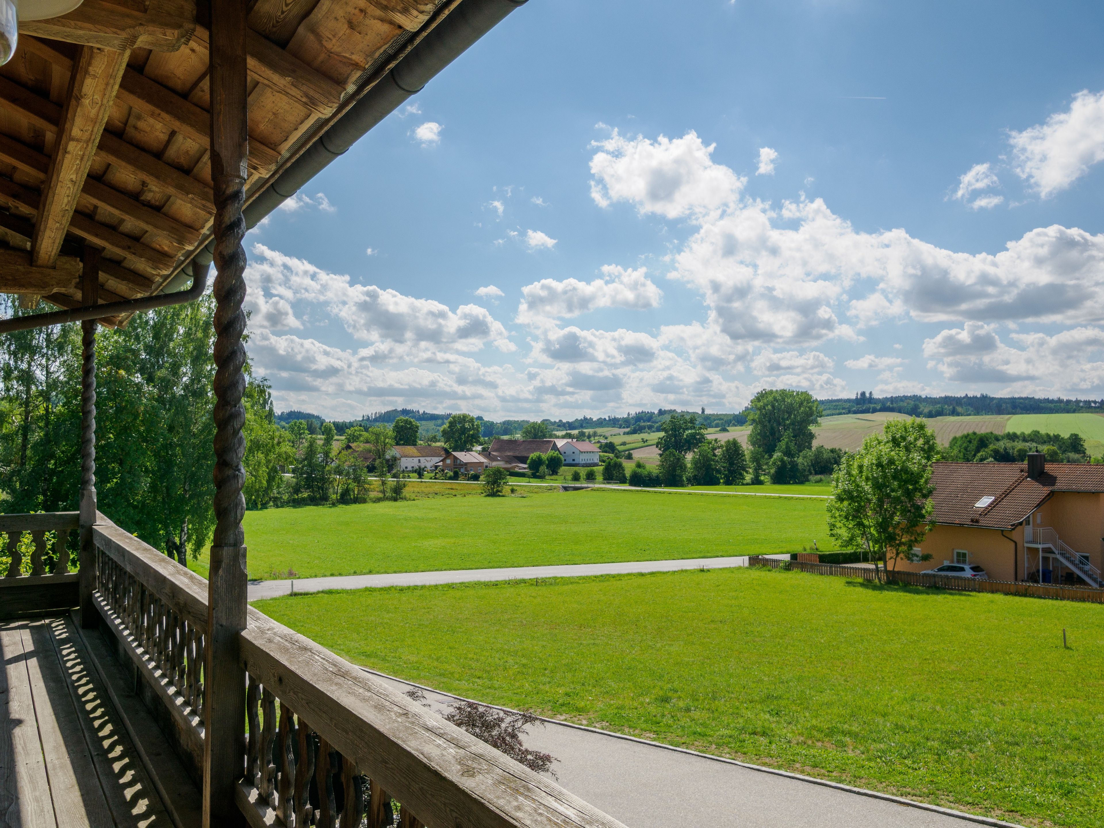 Ein Holzbalkon mit Blick auf ein grünes Feld und Häuser in der Ferne.
