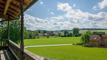 Ein Holzbalkon mit Blick auf ein grünes Feld und Häuser in der Ferne.