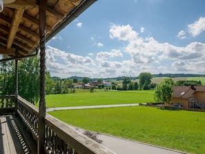 A wooden balcony overlooking a green field with houses in the distance.