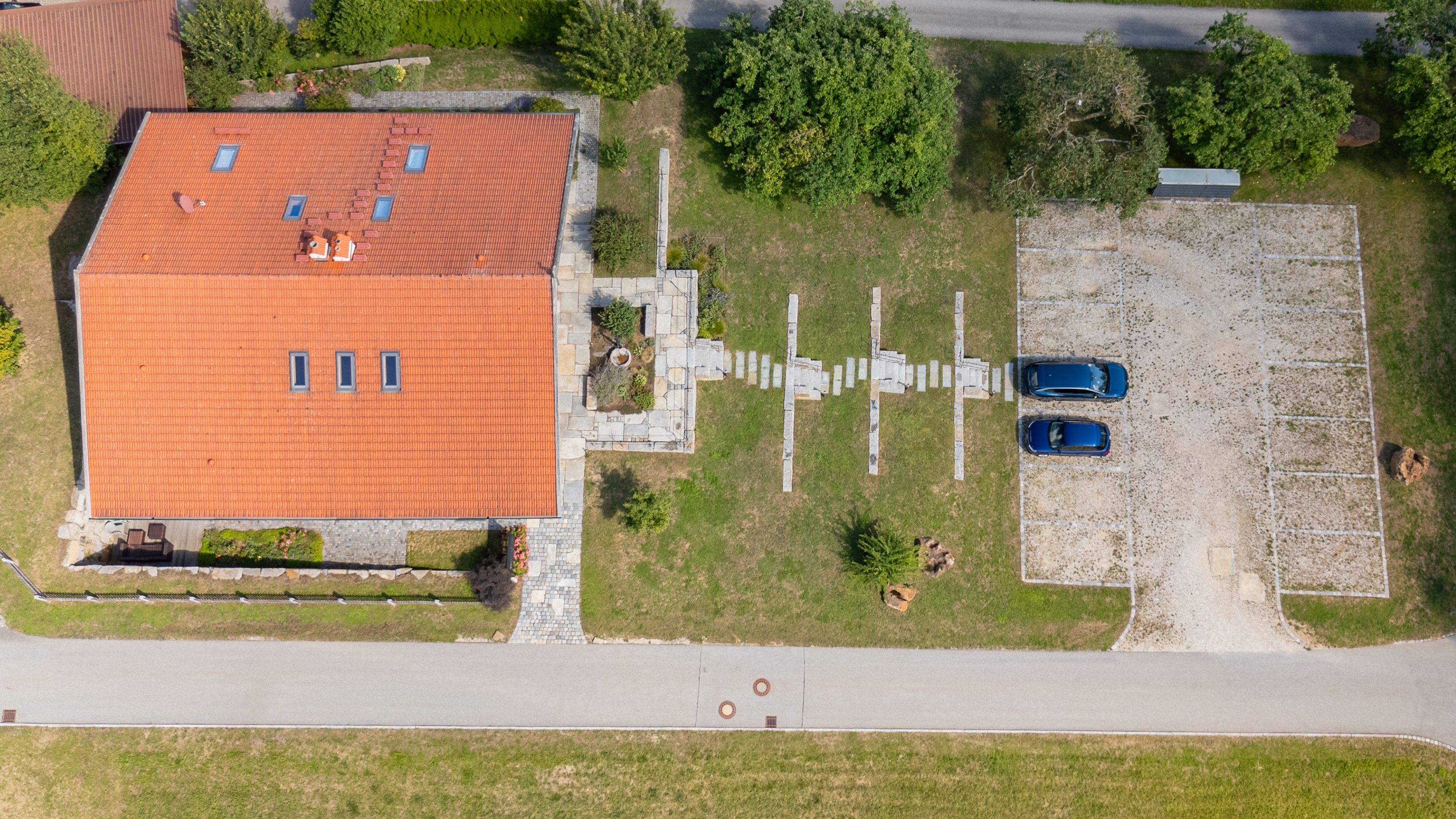 Vue aérienne d’un bâtiment doté d’un toit recouvert de tuiles, d’une allée pavée et de deux voitures garées.