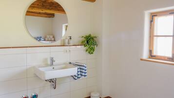 A bathroom with a white sink, a mirror, a towel rack, a potted plant, and a window.
