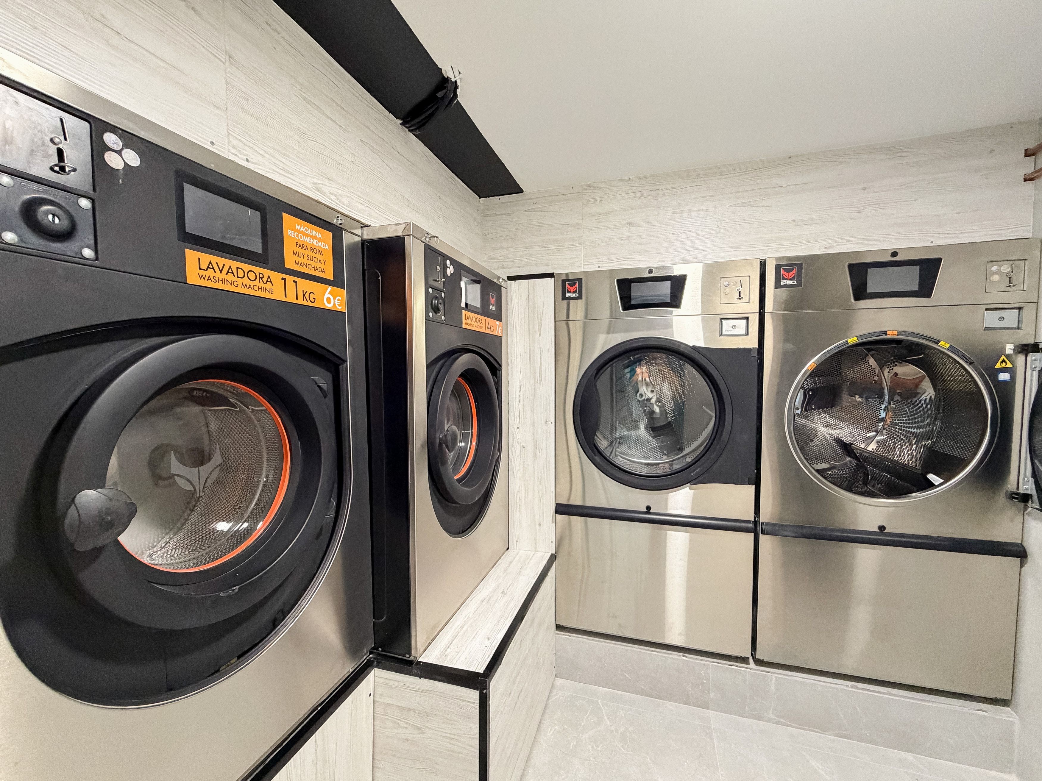 A laundry facility with multiple washing machines, control panels, and a wooden wall.