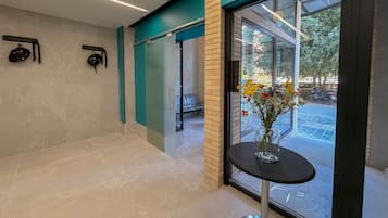 A modern interior with a glass door leading outside, a small table with a vase of flowers, and a bench.