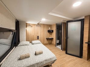 Quarto moderno com cama grande, mesas de cabeceira, guarda-roupa e banheiro com vaso sanitário e chuveiro.