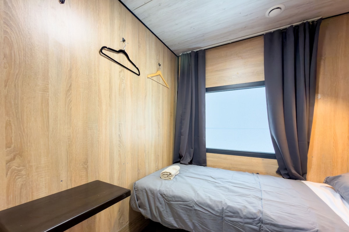 A bedroom with a bed, a bench, a window with curtains, and wooden walls.