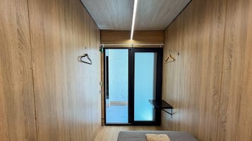 A room with wooden walls, a bed with a grey mattress, and a small black shelf.