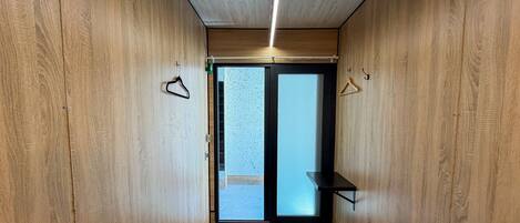 A room with wooden walls, a bed with a grey mattress, and a small black shelf.