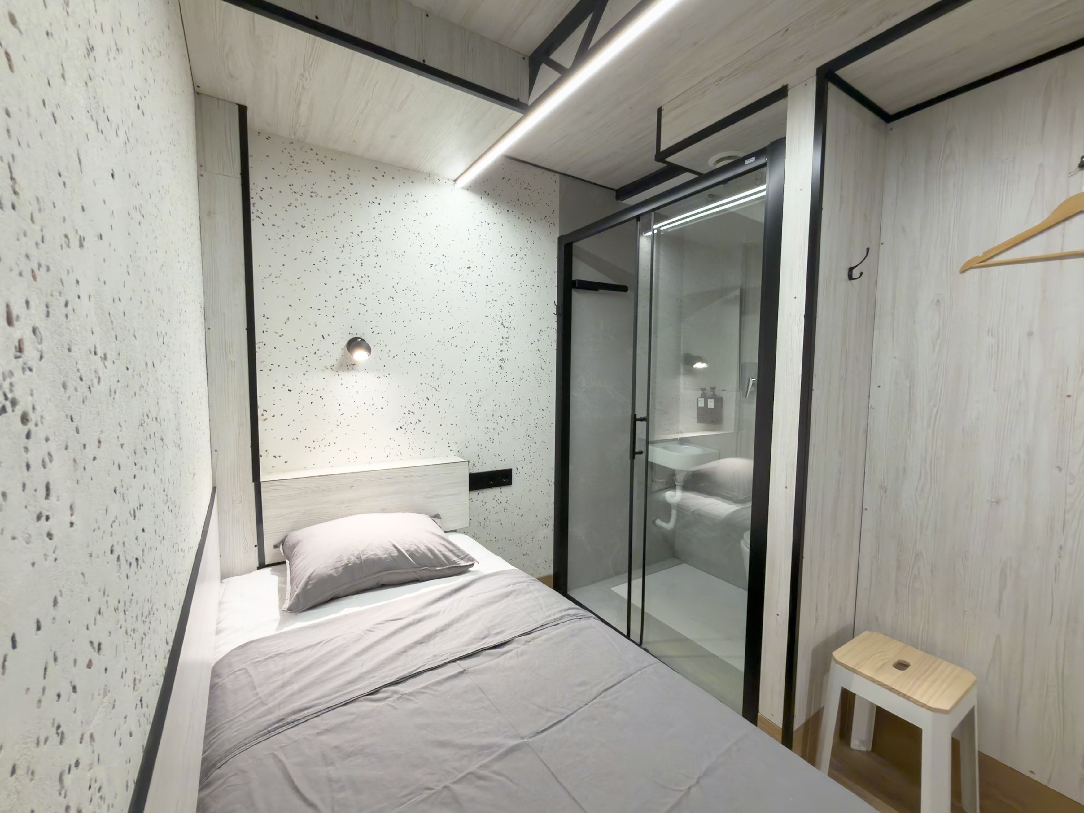 Un dormitorio moderno con cama, un taburete pequeño, cabina de ducha de vidrio y armario de madera.