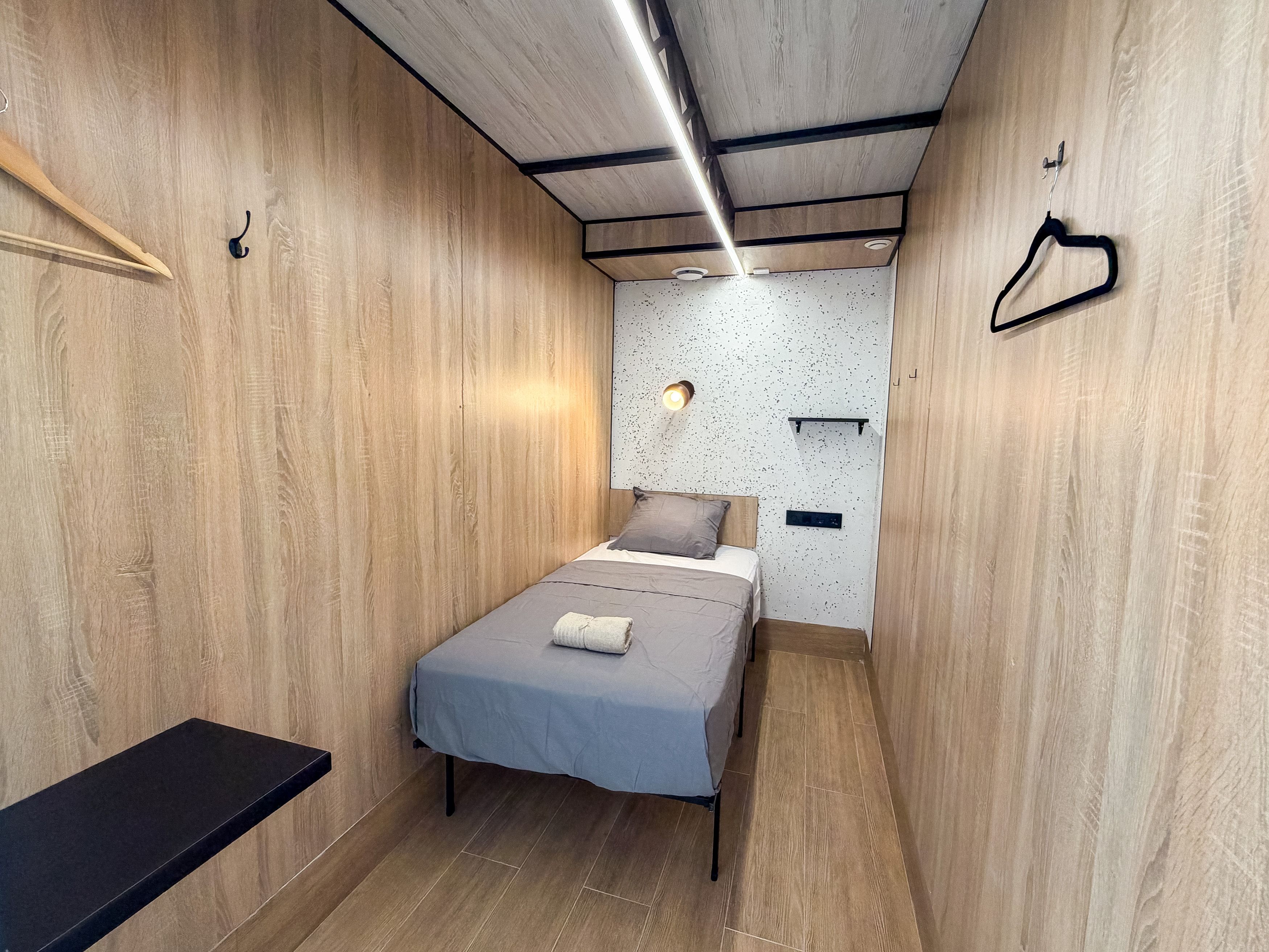 A narrow room with a bed, a bench, and a wall-mounted shelf.