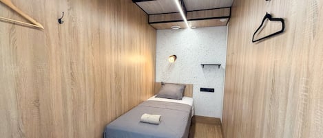 A narrow room with a bed, a bench, and a wall-mounted shelf.