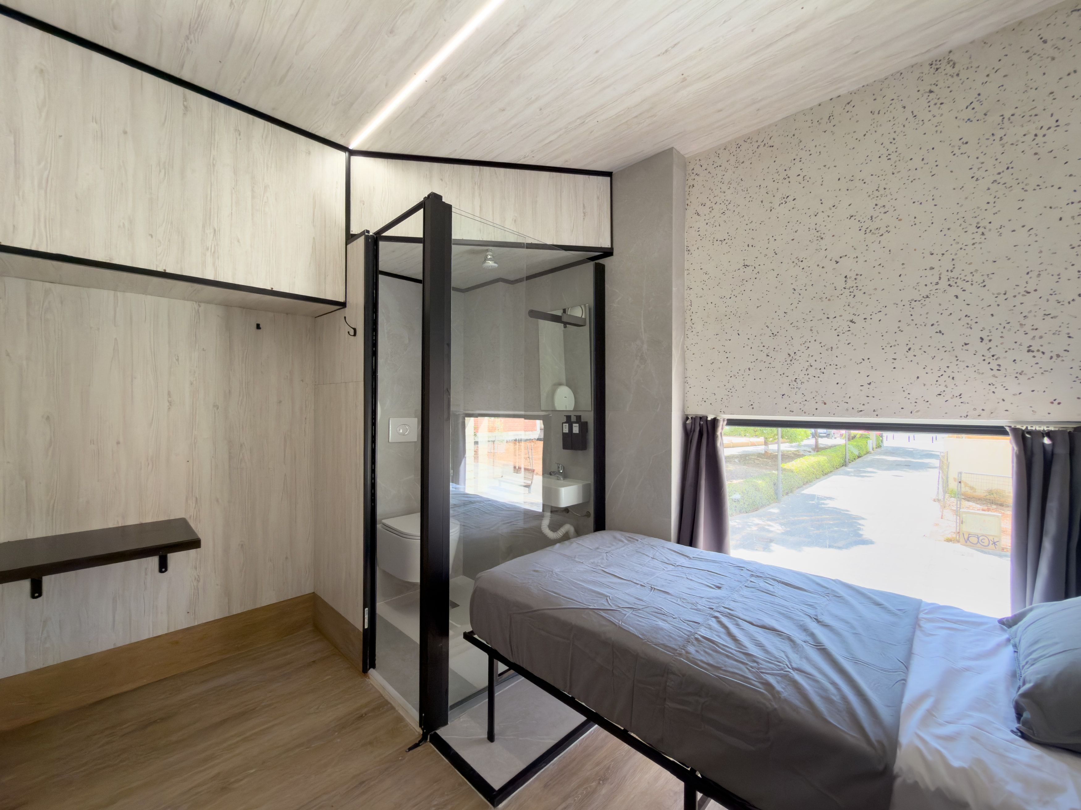 Un dormitorio moderno con cama, zona de ducha y ventana con cortinas.