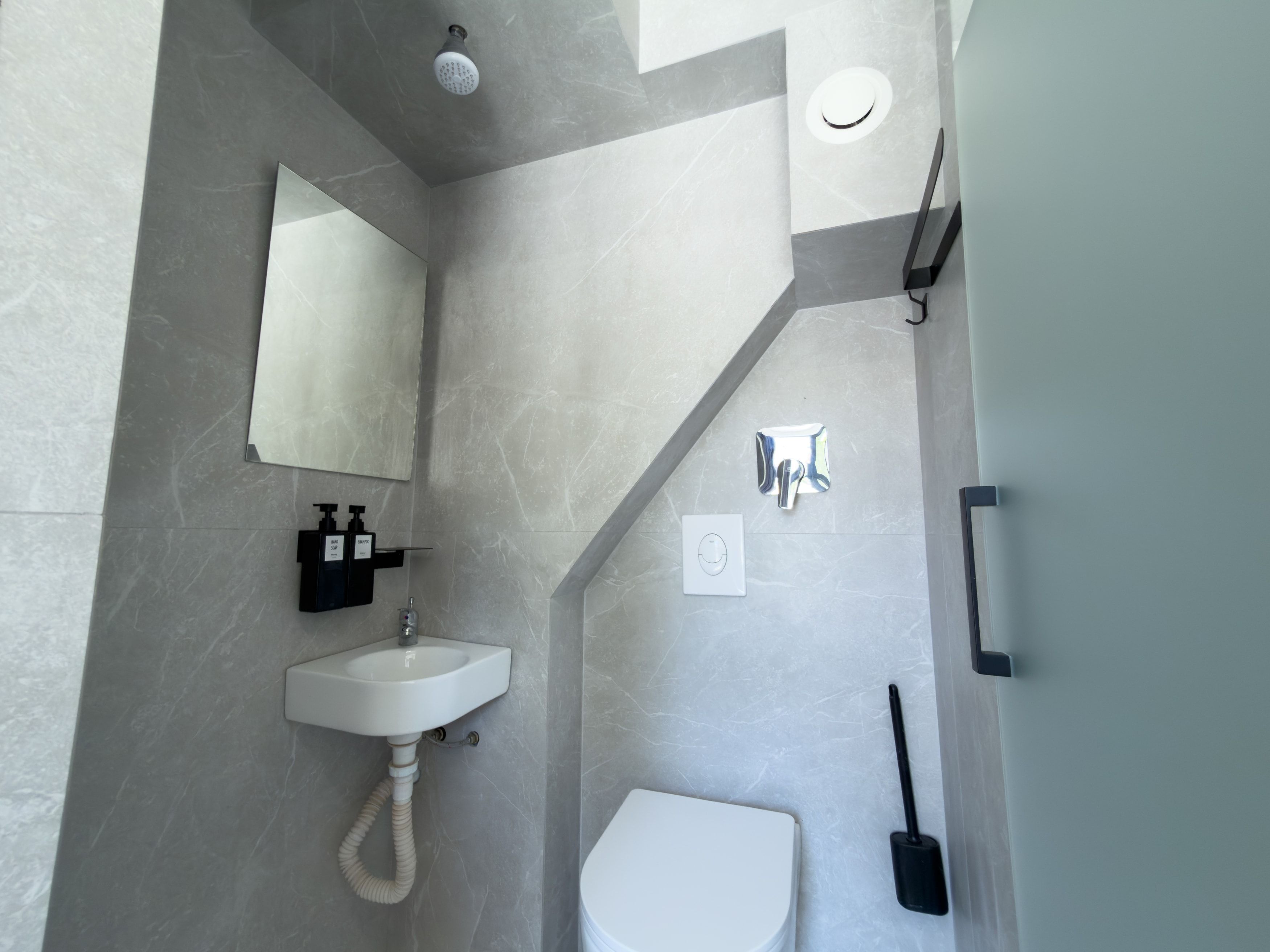 Un baño moderno con un lavabo blanco, un espejo, un cabezal de ducha y un inodoro.