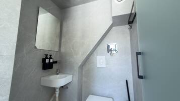 Un baño moderno con un lavabo blanco, un espejo, un cabezal de ducha y un inodoro.