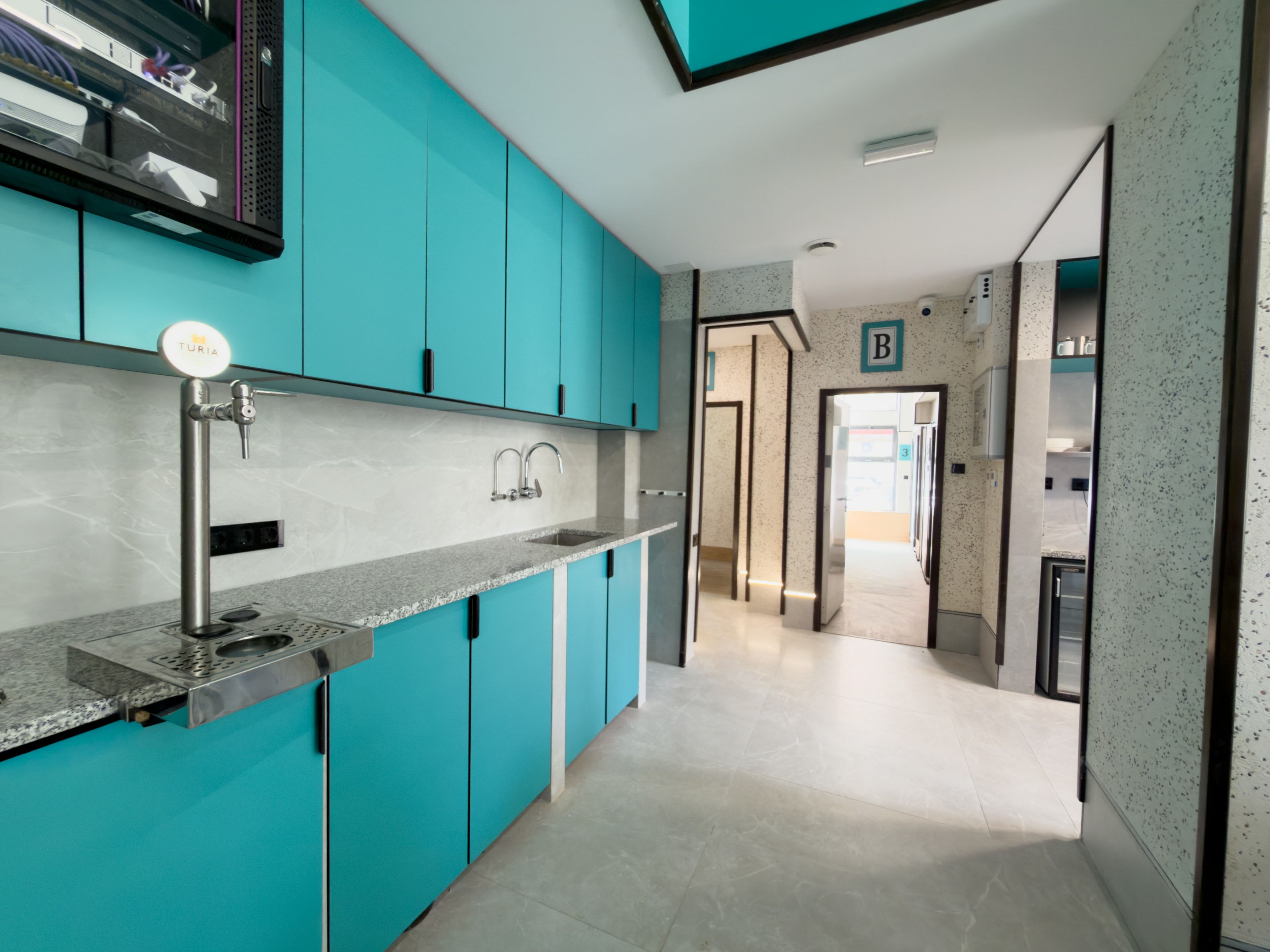 A modern kitchen with teal cabinetry, a stainless steel sink, and a built-in range hood.