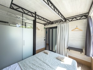A modern bedroom with a bed, a wardrobe, a hanging shower curtain, and a small shelf.