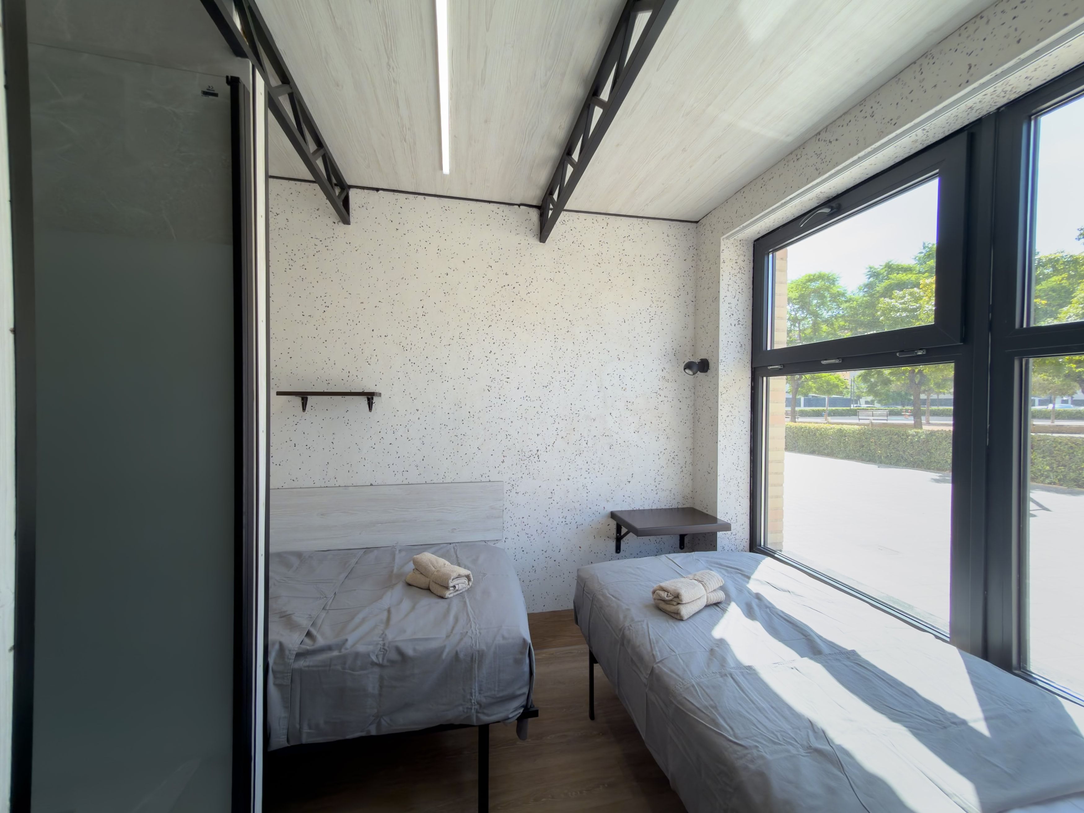 Una habitación con dos camas, una mesita y un ventanal con vistas al exterior.