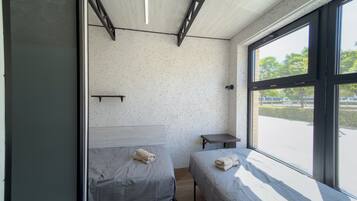 Una habitación con dos camas, una mesita y un ventanal con vistas al exterior.