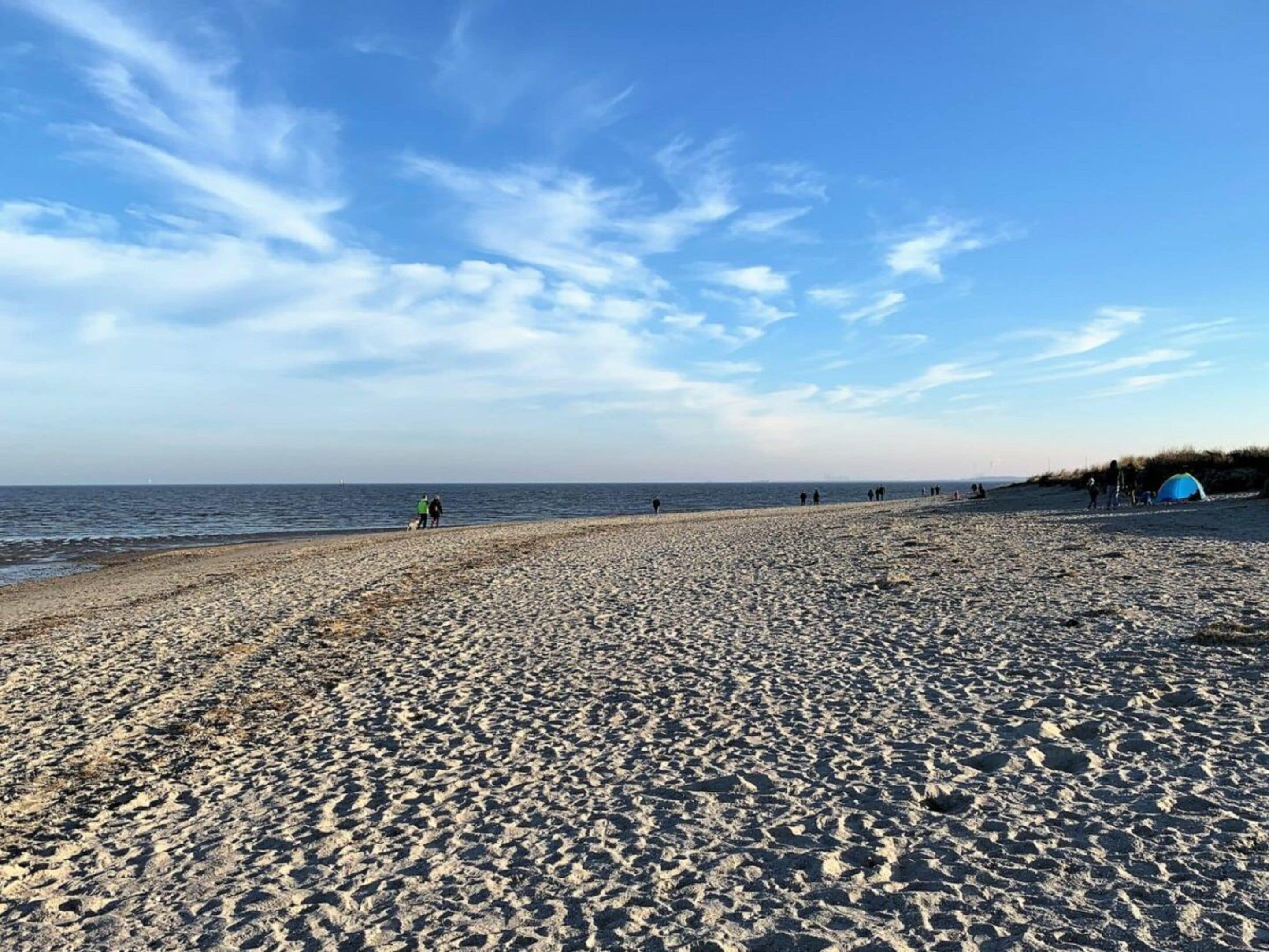 Uma praia com uma tenda e pessoas caminhando pela orla.