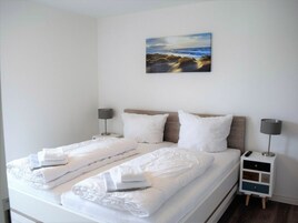 A hotel room with a bed, two bedside tables, a nightstand, and a painting on the wall.