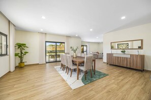 A modern dining area with a wooden table and chairs, a sofa, and a large window with curtains. - Villa Casa do Pomar by Villa Plus (Olhos de Água)
