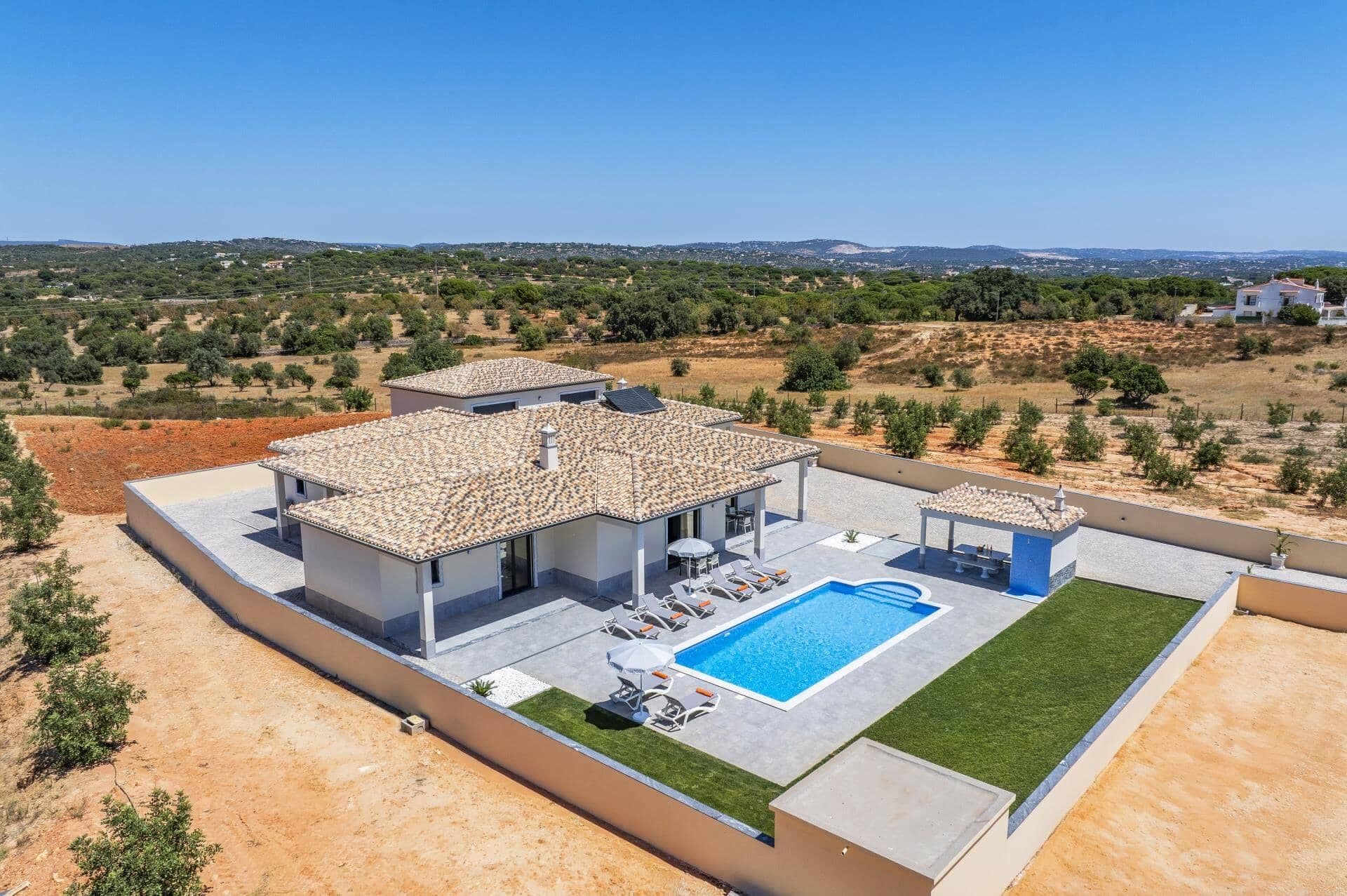 Een modern huis met een zwembad, een overdekt terras en uitzicht op het omliggende landschap.