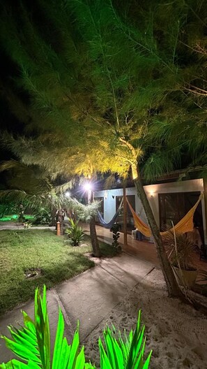 Un espacio al aire libre de noche con una hamaca, un edificio pequeño y un sendero.