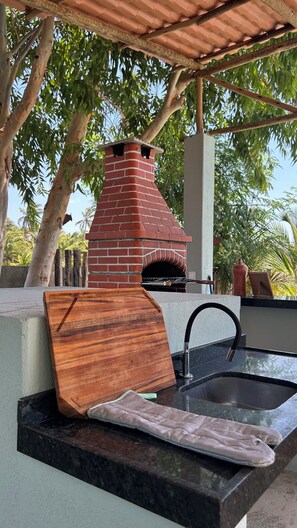 Una cocina exterior con horno de ladrillo, tabla de cortar de madera y pileta.