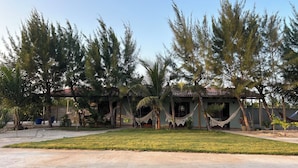 A building with a covered patio area, surrounded by trees and a grassy lawn.