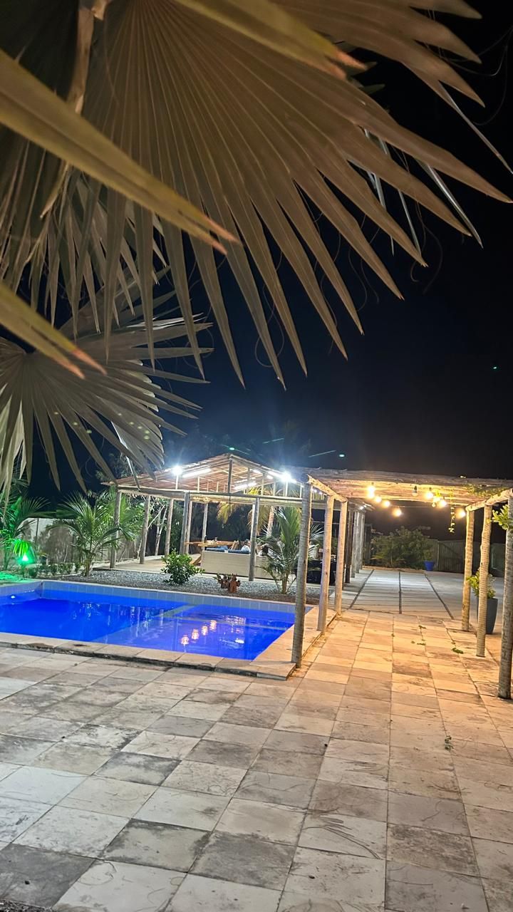 Área externa noturna com piscina, espaço de estar coberto e um caminho.