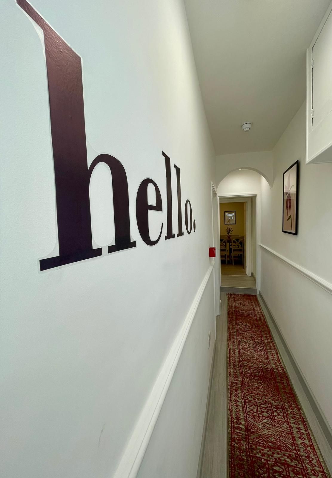 A hallway with a large 'hello' sign on the wall, leading to a room with a door at the end.