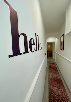 A hallway with a large 'hello' sign on the wall, leading to a room with a door at the end. - Ridgeways Premium House (Bristol)
