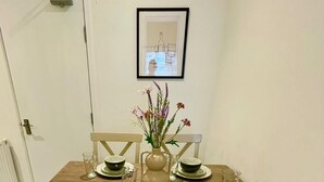 Uma mesa de jantar com quatro cadeiras, um vaso com flores e um quadro na parede.