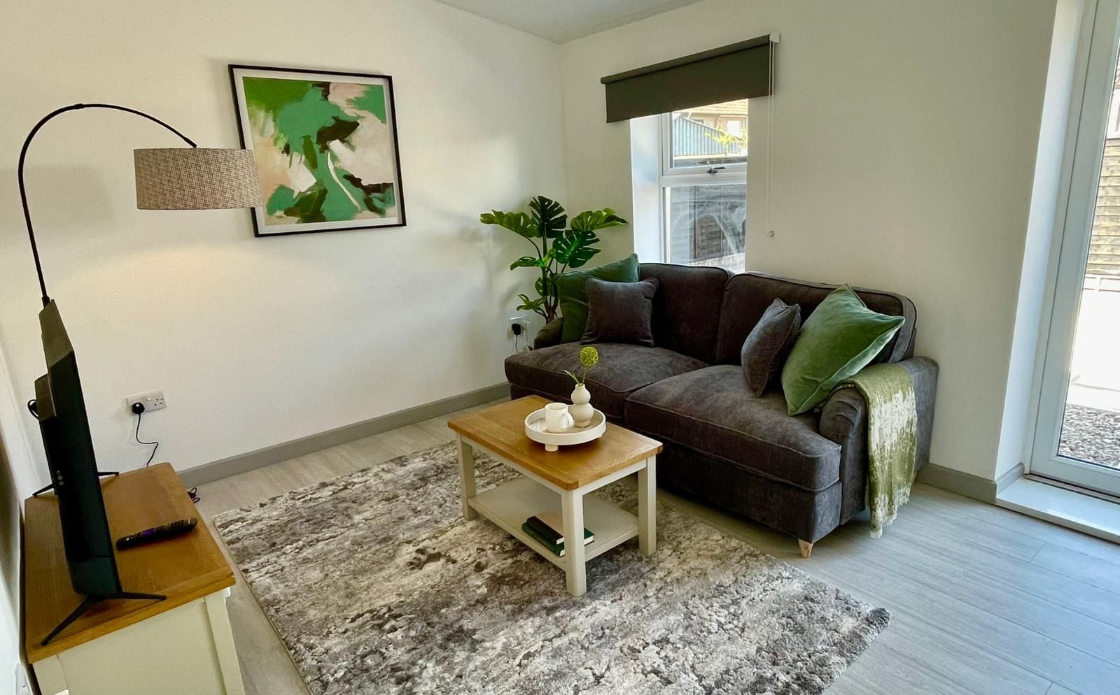 Una sala de estar con sofá, mesa de centro, cuadro, planta y lámpara.