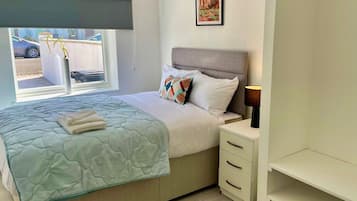 Un dormitorio con cama, mesita de noche, lámpara y ventana con vistas al exterior.