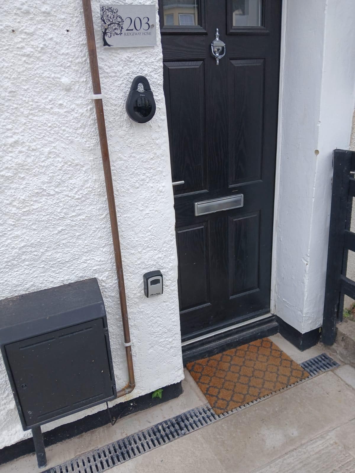Una puerta negra con cerradura electrónica, un buzón y una placa con el número 203 Ridgeway Home.