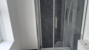 Casa de banho moderna com cabine de duche em vidro, sanita branca e bancada preta.
