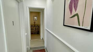A hallway with a red patterned carpet, white walls, and a framed artwork of a purple flower.