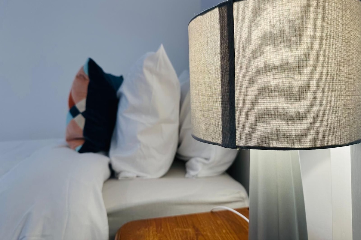 A bed with white bedding and a black and white checkered lamp shade.