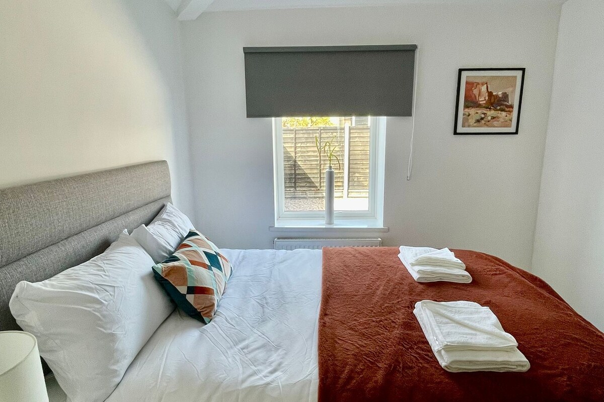 A bedroom with a bed, pillows, a bedside table, a window with a view, and a painting on the wall.