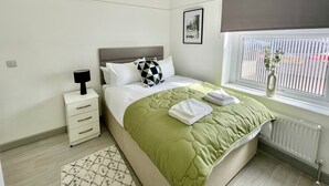 Quarto moderno com cama, mesa de cabeceira, luminária e janela com persianas.
