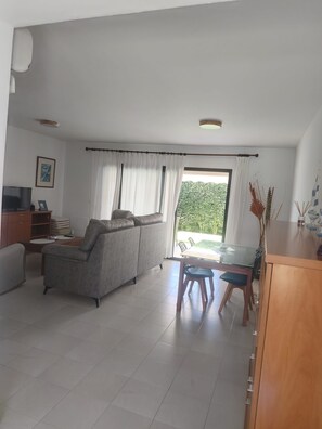 A spacious living area with a sofa, a TV, and a dining table with chairs. - Casa Luz Relax (El Rompido)