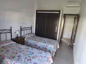 A bedroom with two beds, a nightstand, a lamp, and a wardrobe.