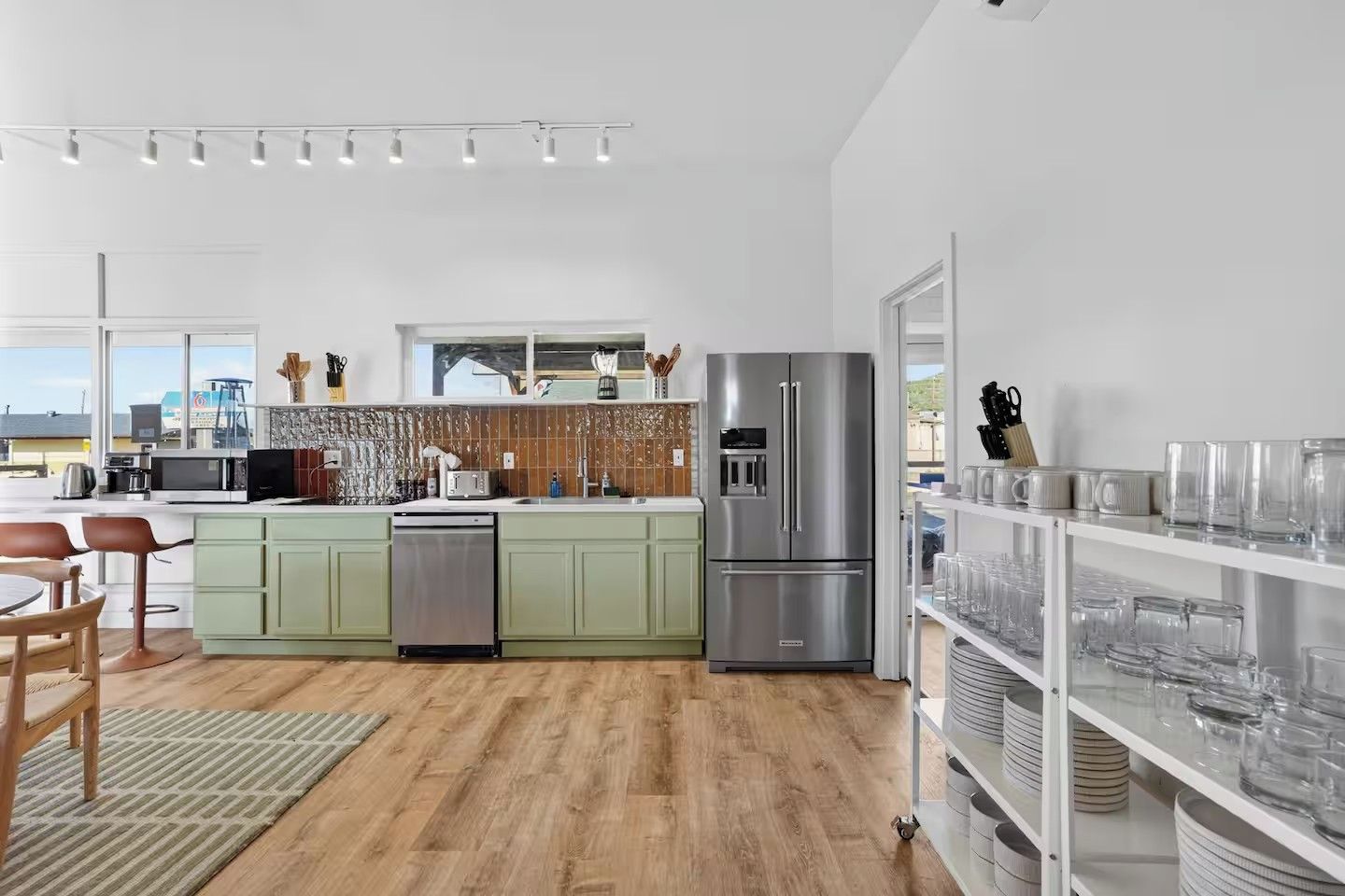 A modern kitchen with a stainless steel refrigerator, a dishwasher, and a microwave. There is a dining area with a table and chairs.