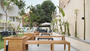 An outdoor seating area with wooden tables and chairs, surrounded by potted plants and a white umbrella. - 88 by spacey (cairo)