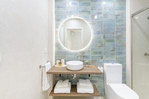 Un bany amb un mirall rodó, un lavabo i un vàter.